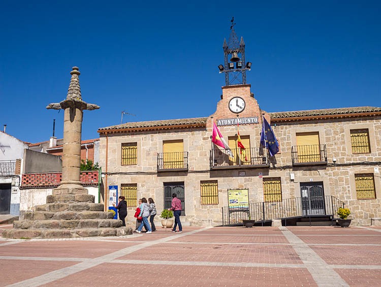 Fachada de piedra del Ayuntamiento en la Plaza de la Constitución, con su torre del reloj, banderas en el balcón y el rollo de piedra a la izquierda