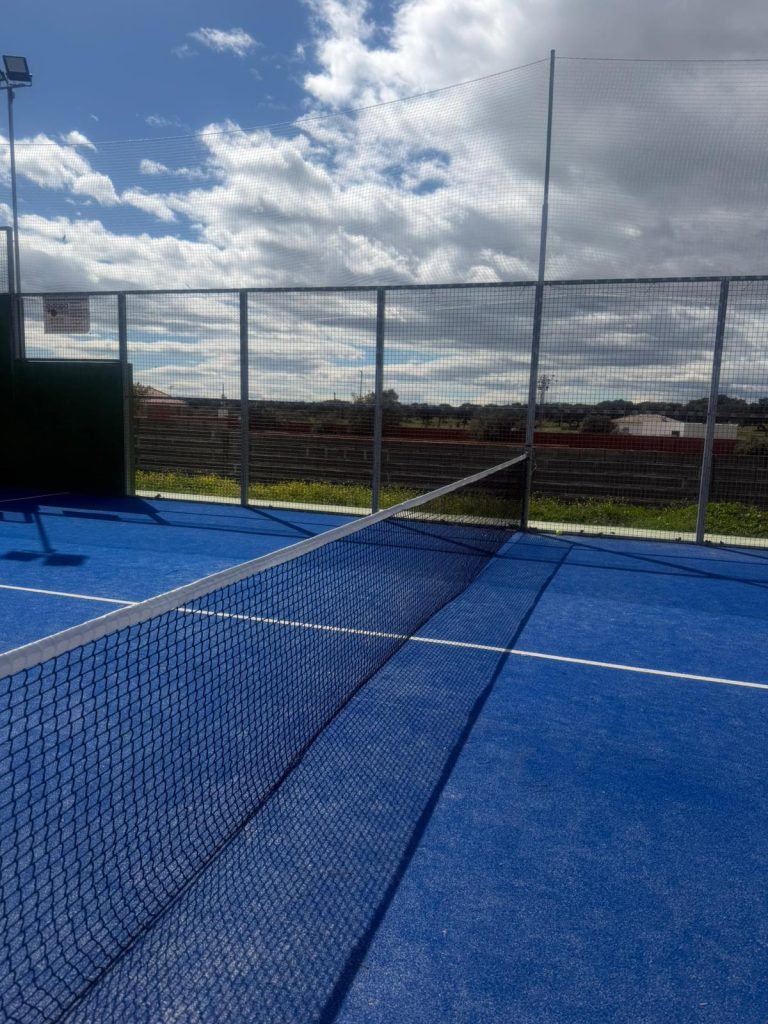 Pista de pádel municipal de césped azul, con la red y el cerramiento de malla
