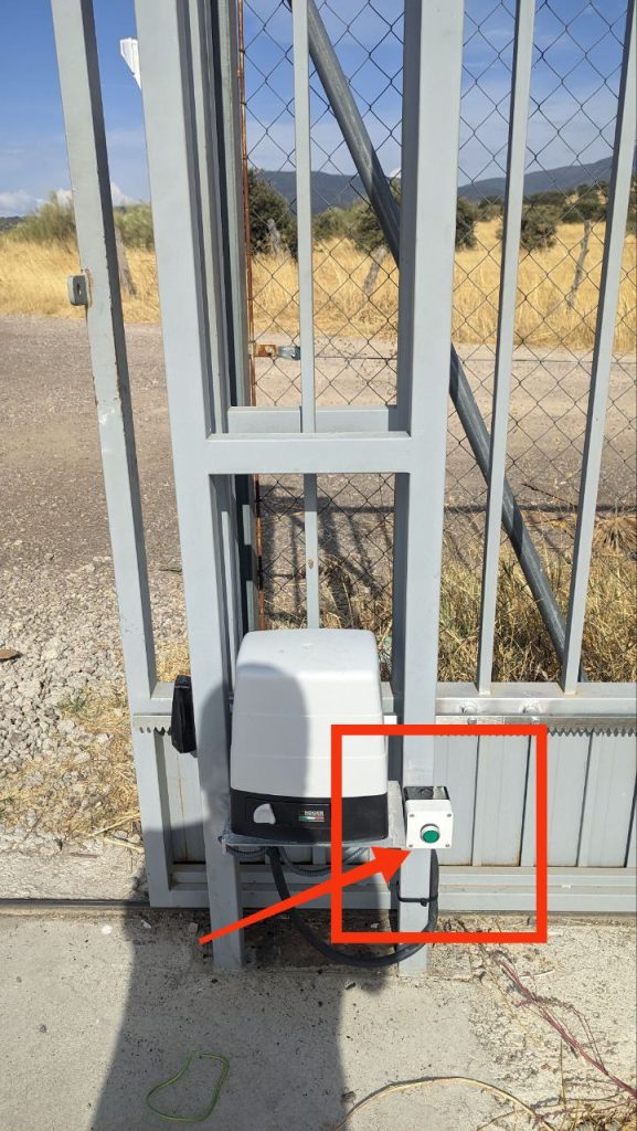 Puerta del punto limpio con el botón verde de salida señalado en rojo